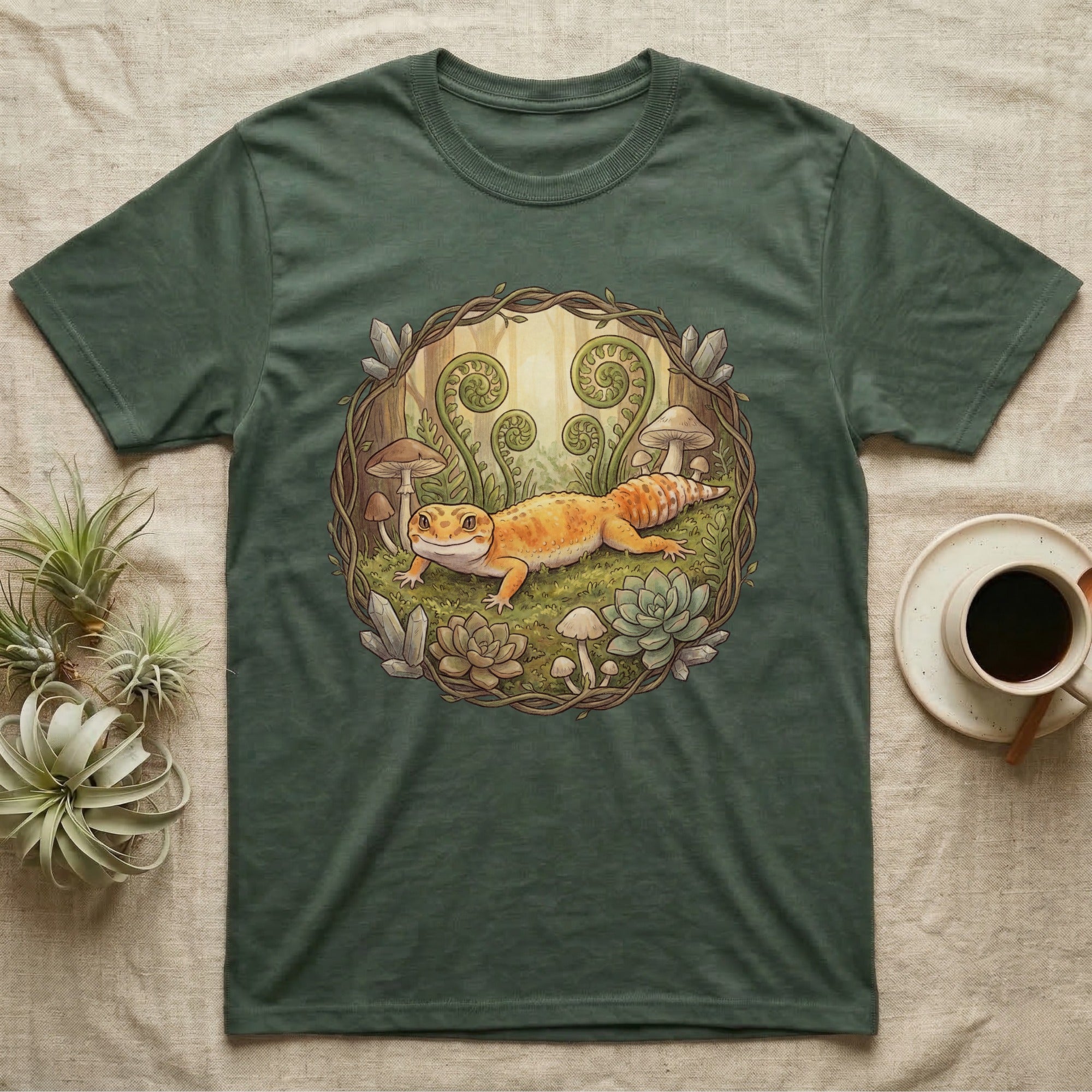 Green t-shirt with a gecko and succulents design in a forest clearing.