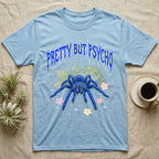 Cobalt Blue Tarantula Feral T-Shirt in Light Blue — Cobalt blue tarantula with electric-blue legs under jagged cobalt metal text PRETTY BUT PSYCHO with pastel blossoms