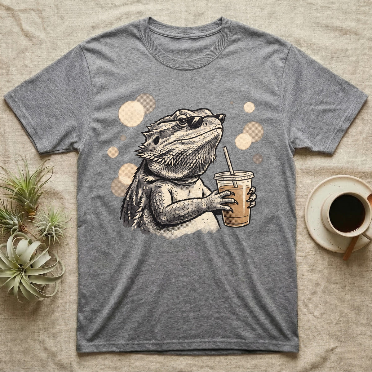 Cold Brew Bearded Dragon T-Shirt in Sport Grey — Flat near-photoreal illustration of a bearded dragon in tiny sunglasses holding a cold brew with warm bokeh.