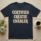 Certified Crestie Enabler T-Shirt in Navy — Bold retro drop-shadow wordmark reading "Certified Crestie Enabler" in cream and ochre on a grey background.