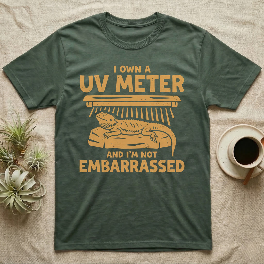 Reptile Keeper UV Meter T-Shirt in Military Green — Linocut block-print badge of a UVB tube lamp above an empty basking rock, ringed by carved slogan lettering.