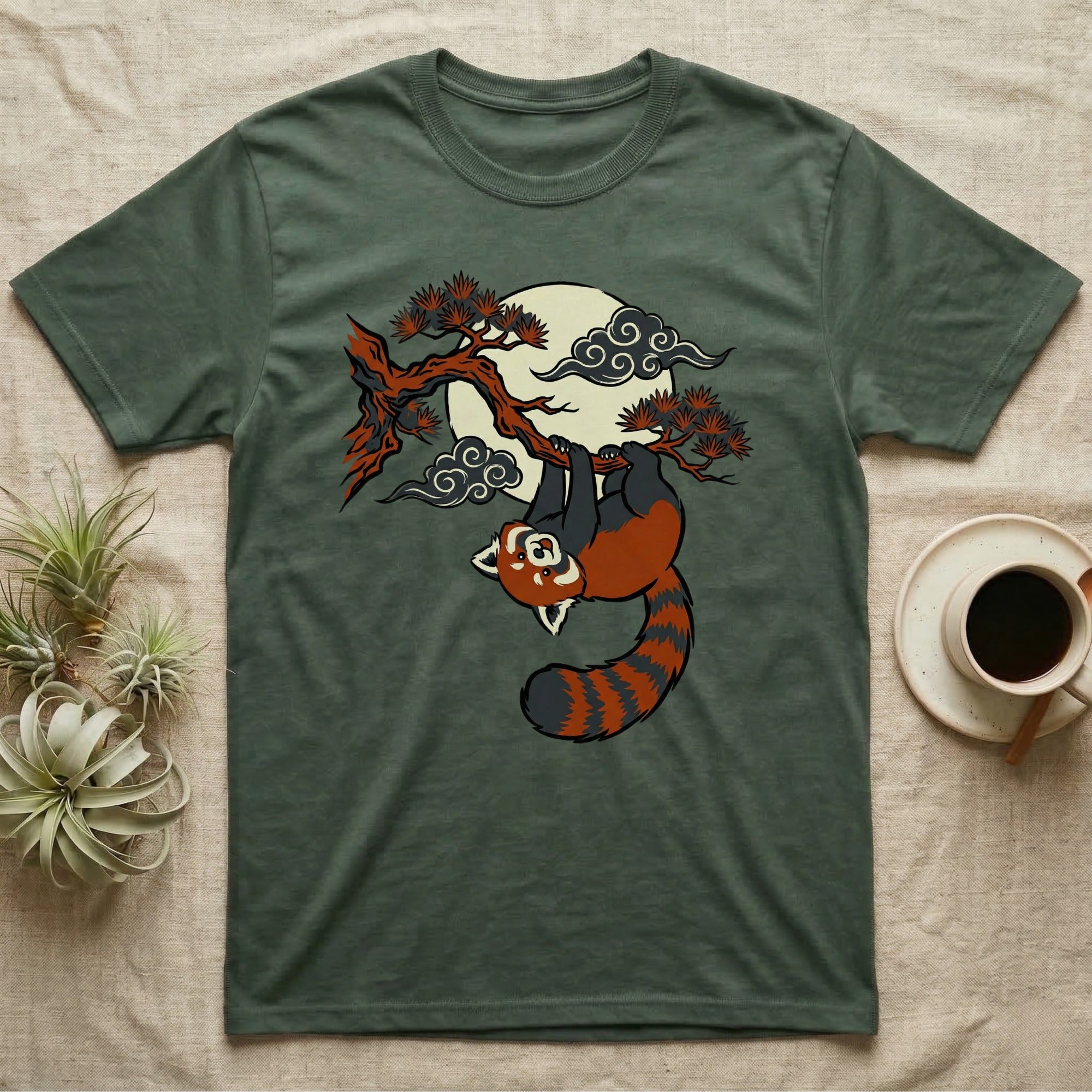 Green t-shirt with a red panda hanging from a tree branch under a moon.