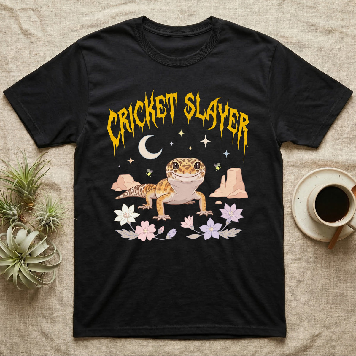 Leopard Gecko Feral T-Shirt in Black — Smiling leopard gecko in a pastel desert-night scene under a spiky golden metal wordmark reading CRICKET SLAYER.