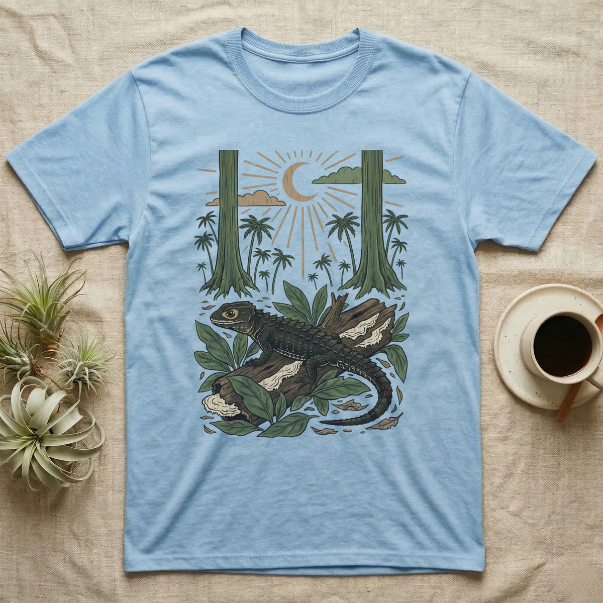 Crocodile Skink Home Range T-Shirt in Light Blue — Woodcut-style illustration of a red-eyed crocodile skink crouched on a rainforest log among broad leaves and palms, no on-shirt text.