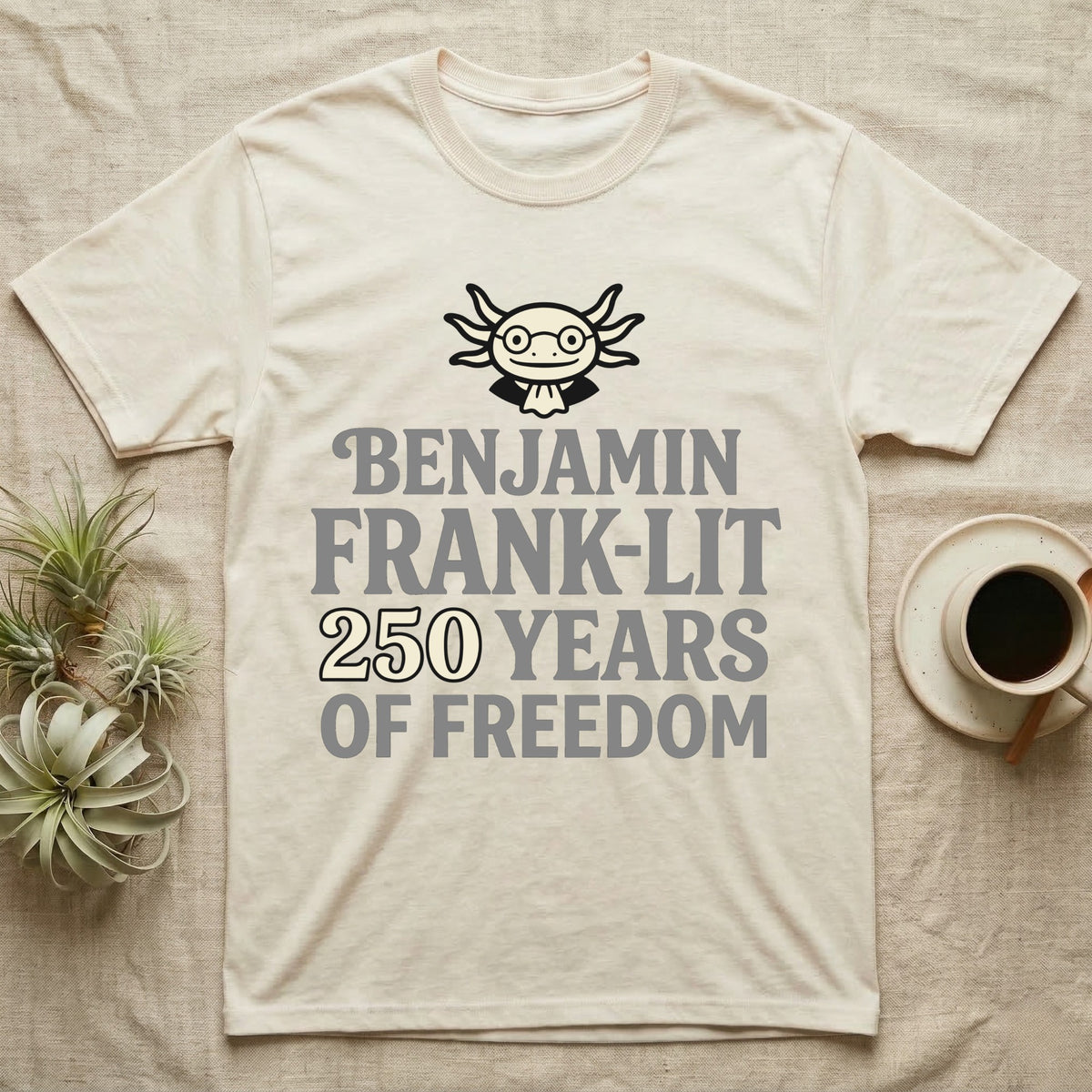 Axolotl Benjamin Franklin T-Shirt in Natural — Flat cream axolotl as Ben Franklin in glasses above bold text reading Benjamin Frank-Lit, 250 Years of Freedom.