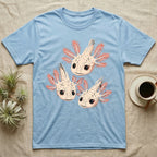 Vintage comic screen-print illustration of three axolotls clustered together with coral feathery gills and sparkling star-highlighted eyes, graphic-only, no text. — shown on a Light Blue tee.