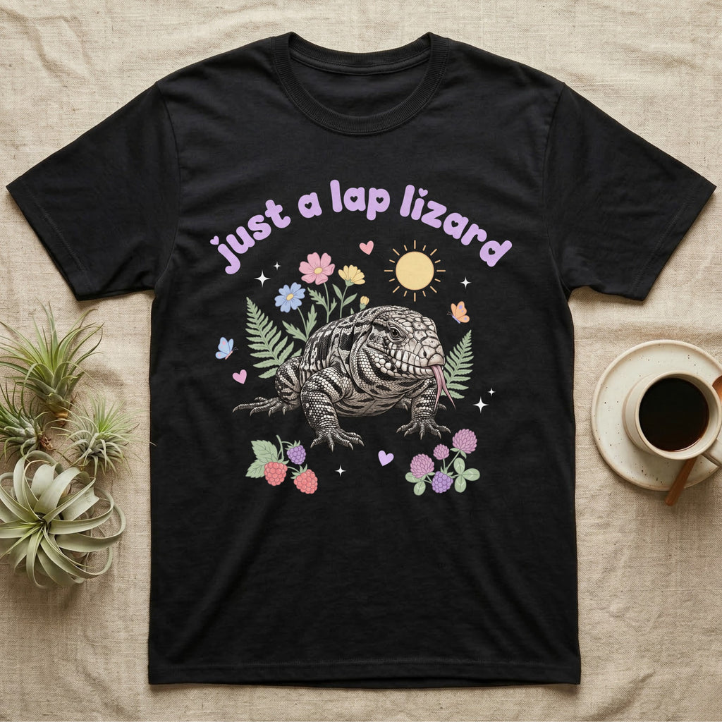 Argentine Tegu Baby T-Shirt in Black — Black-and-white Argentine tegu with forked tongue among pastel flowers under puffy lavender text "just a lap lizard".