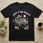 Argentine Tegu Baby T-Shirt in Black — Black-and-white Argentine tegu with forked tongue among pastel flowers under puffy lavender text "just a lap lizard".