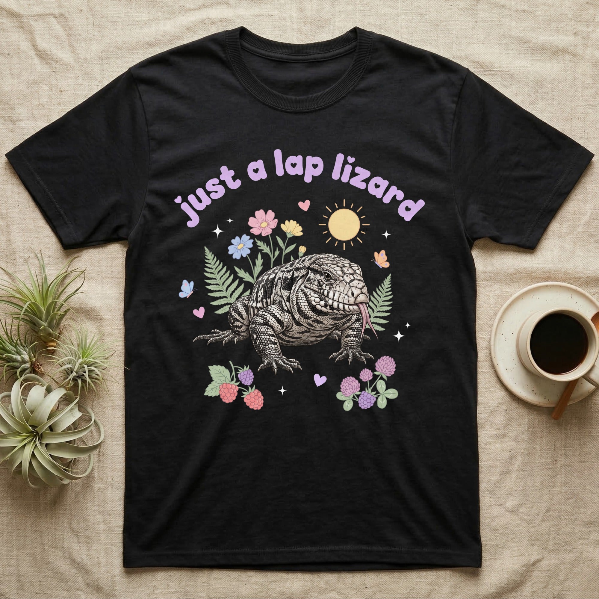 Argentine Tegu Baby T-Shirt in Black — Black-and-white Argentine tegu with forked tongue among pastel flowers under puffy lavender text "just a lap lizard".