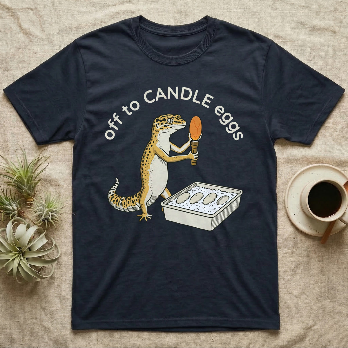 Leopard Gecko Candling T-Shirt in Navy — Leopard gecko holding a torch under a glowing orange egg beside a tub of eggs, under the words off to CANDLE eggs