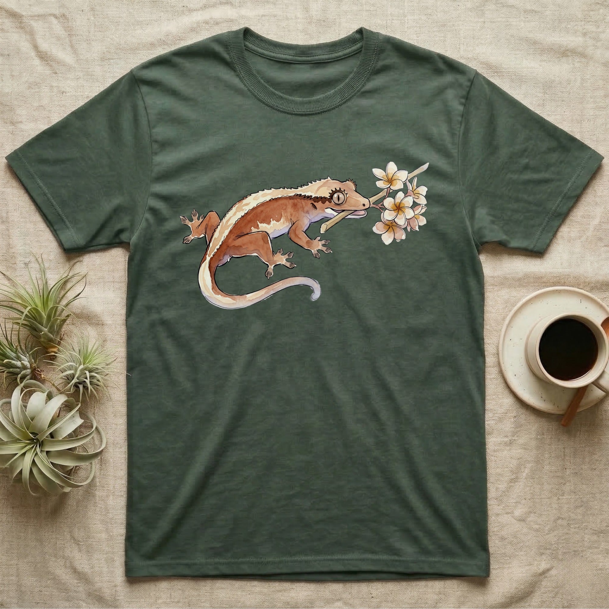 Crested Gecko Blossom T-Shirt in Military Green — Watercolor illustration of a rust-brown crested gecko holding a frangipani blossom sprig, on a dark grey t-shirt.