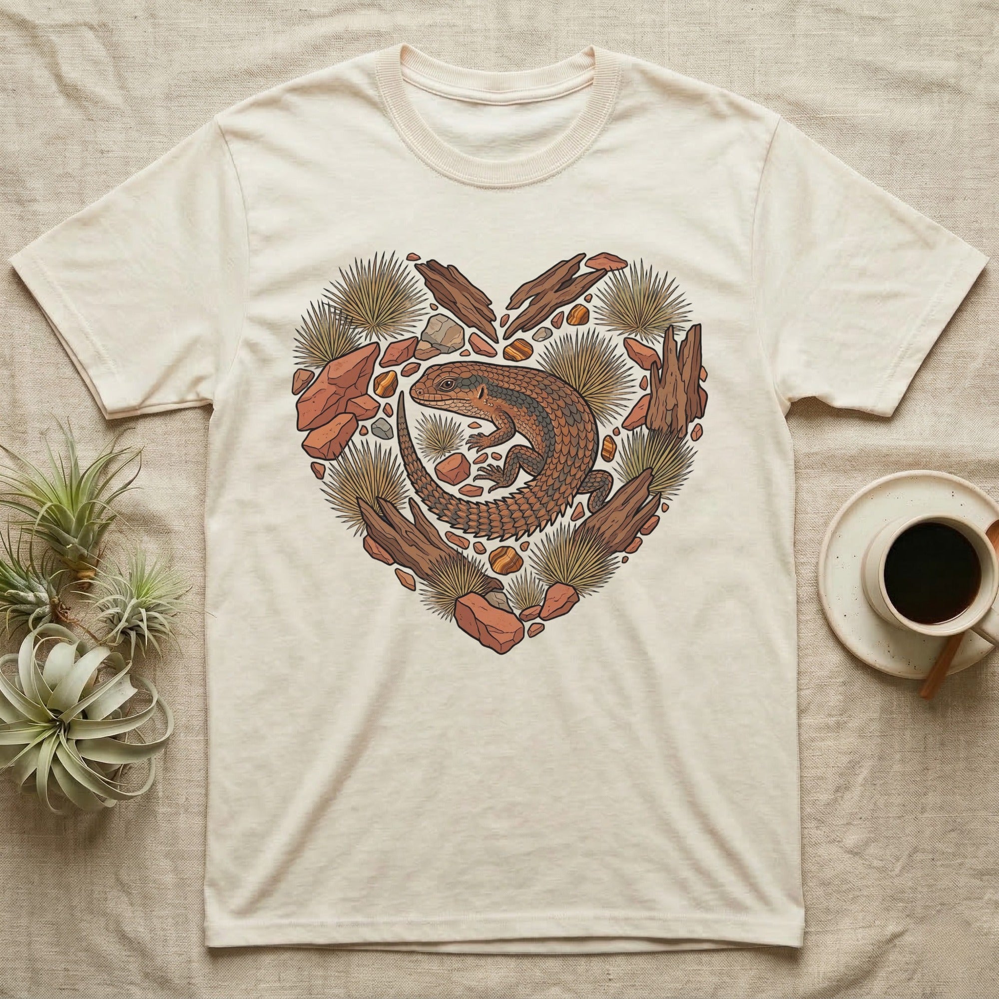 Cream t-shirt with a heart-shaped design of a lizard, rocks, and desert plants.