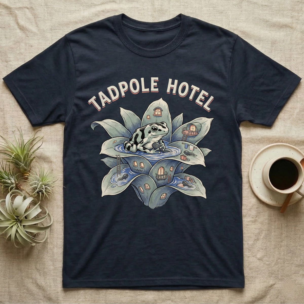 Tadpole Hotel Frog T-Shirt in Navy — Whimsical naturalist illustration of a dart frog tucking tadpoles into a bromeliad Tadpole Hotel with hand-lettered marquee text.