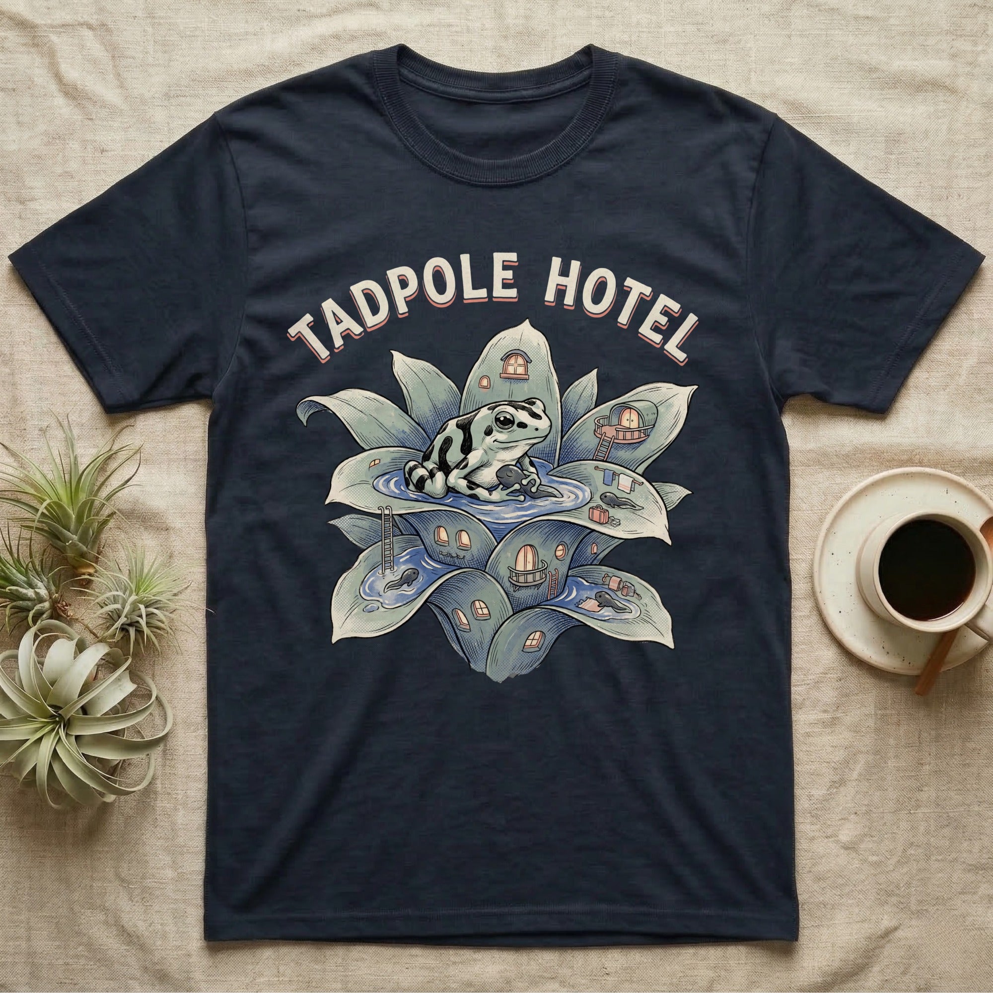 Tadpole Hotel Frog T-Shirt in Navy — Whimsical naturalist illustration of a dart frog tucking tadpoles into a bromeliad Tadpole Hotel with hand-lettered marquee text.