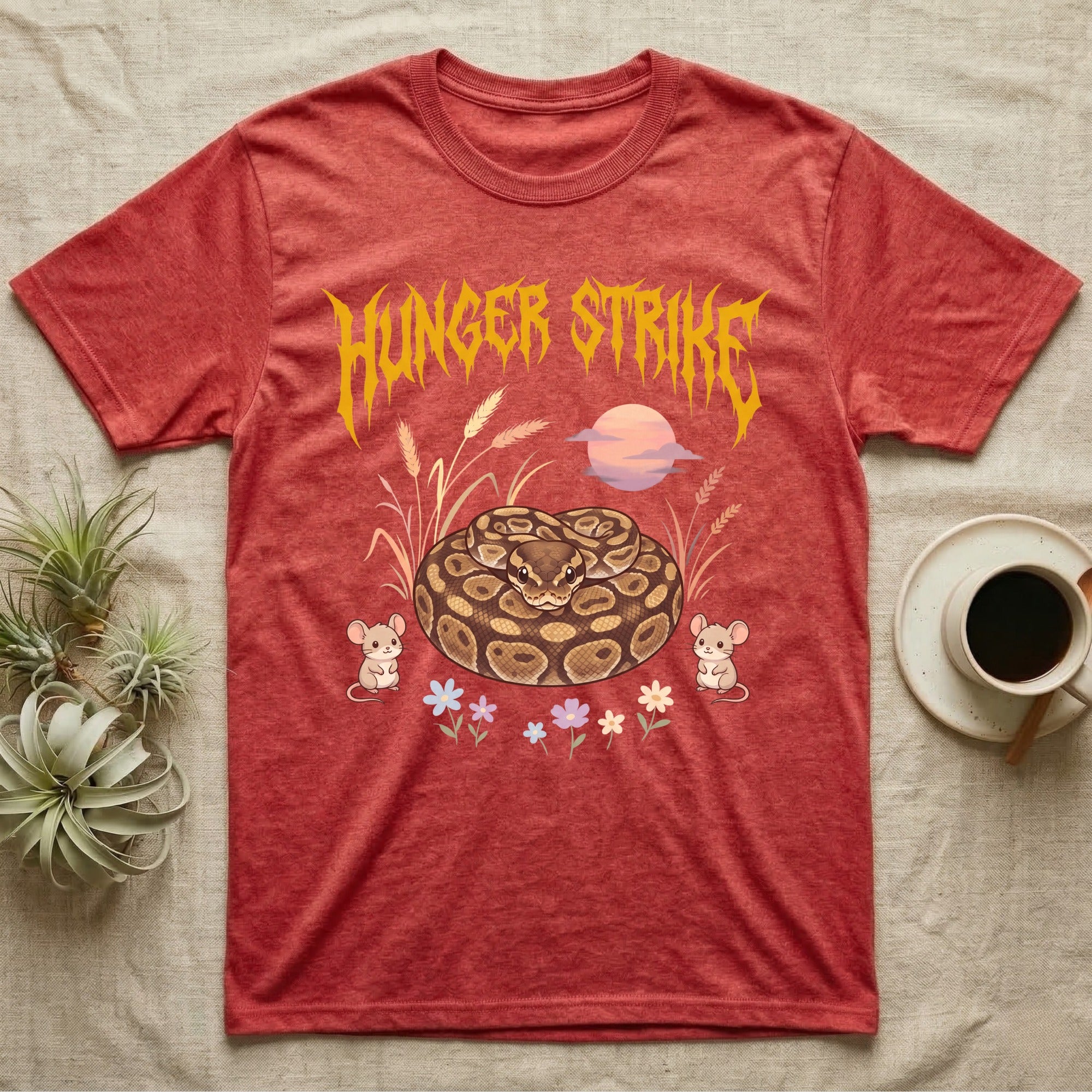 Ball Python Feral T-Shirt in Heather Red — Ball python coiled in a loaf in a pastel savanna scene under a spiky honey-gold metal wordmark reading HUNGER STRIKE.