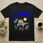 Northern Blue-Tongue Skink Feral T-Shirt in Black — Blue-tongue skink with its blue tongue out under a jagged cobalt-blue metal "ALL BLUFF" wordmark and pastel leaves.