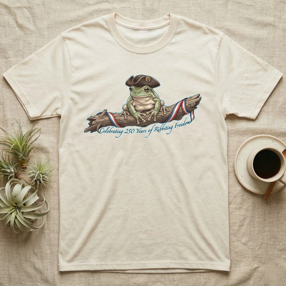 Tree Frog Freedom T-Shirt in Natural — Detailed green tree frog in a tricorn hat on a ribboned branch under script Celebrating 250 Years of Freedom.