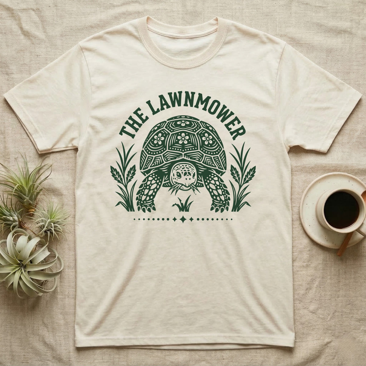 Sulcata Tortoise Under Lawn T-Shirt in Natural — Engraved sulcata tortoise in white line, head down and legs braced mid-dig, under retro script reading UNDER THE LAWN.