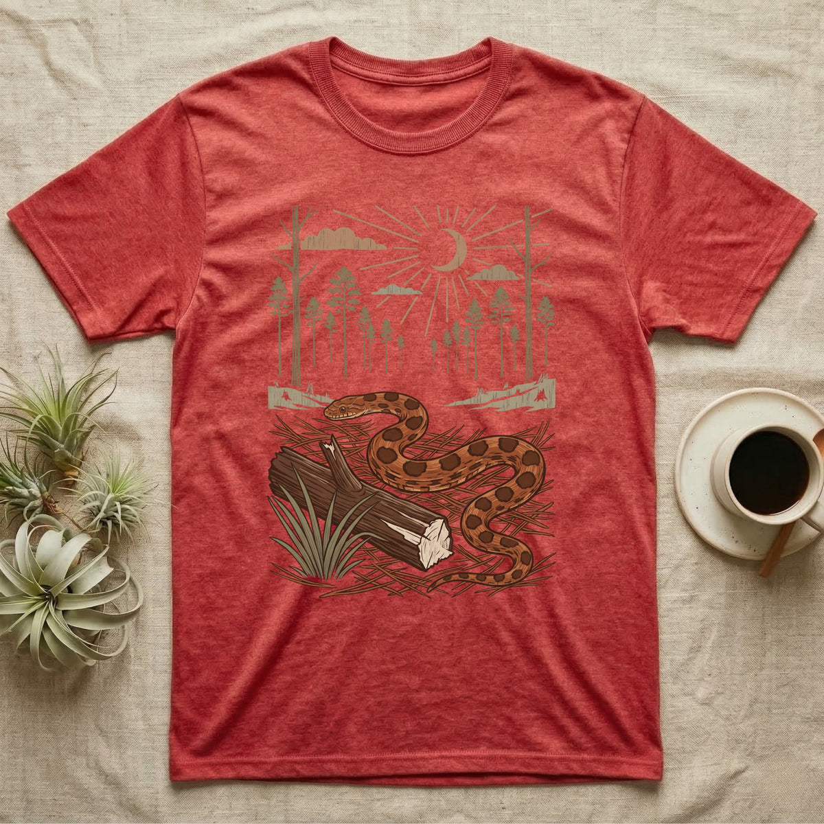 Corn Snake Home Range T-Shirt in Heather Red — Woodcut-style illustration of a corn snake winding across pine straw beside a split log with pine trees behind, no on-shirt text.