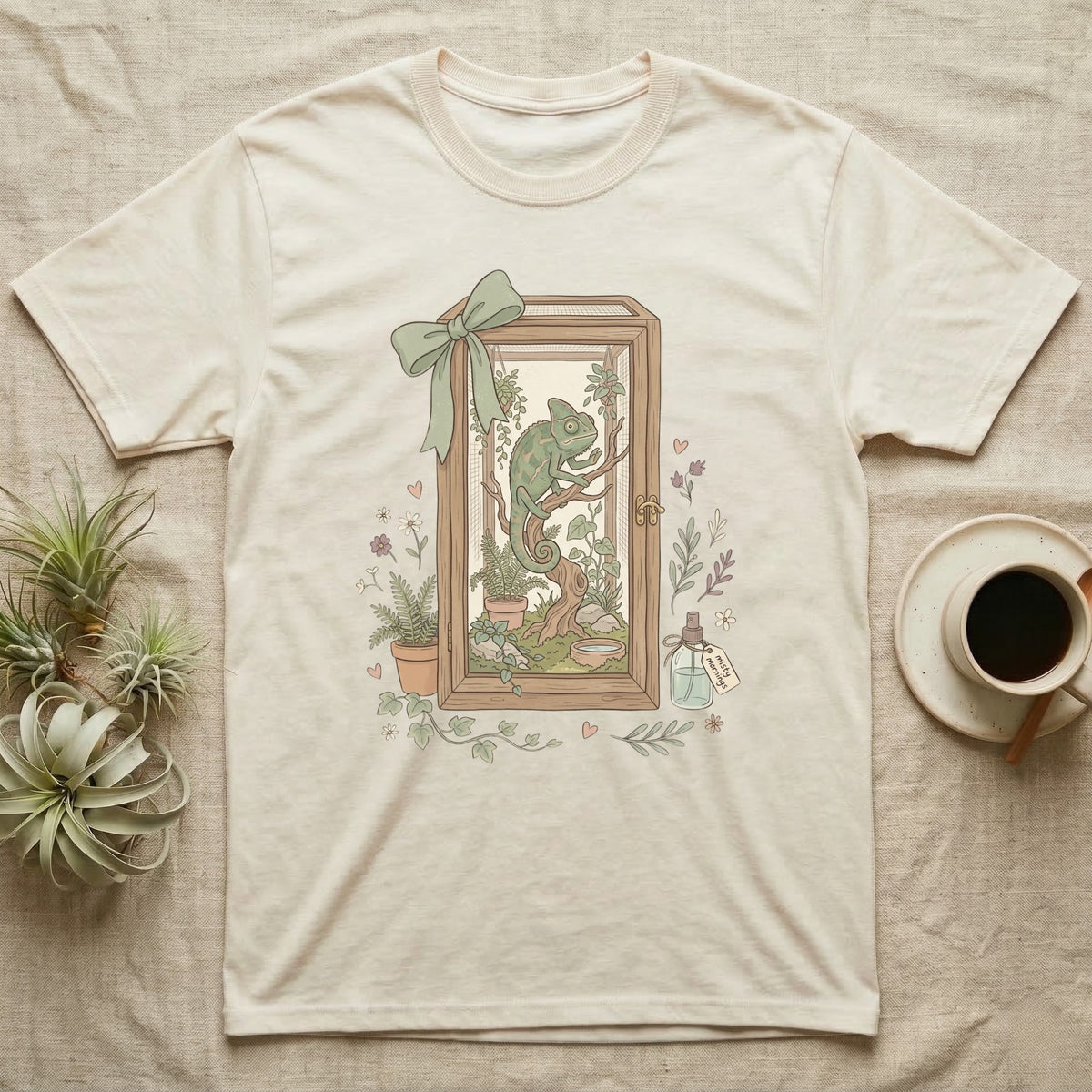 Cream t-shirt with framed illustration of a chameleon in a terrarium.
