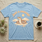 Kenyan Sand Boa Softie T-Shirt in Light Blue — Kenyan sand boa looping out of pastel sand dunes under a puffy "just a sausage" bubble wordmark with tiny hearts.