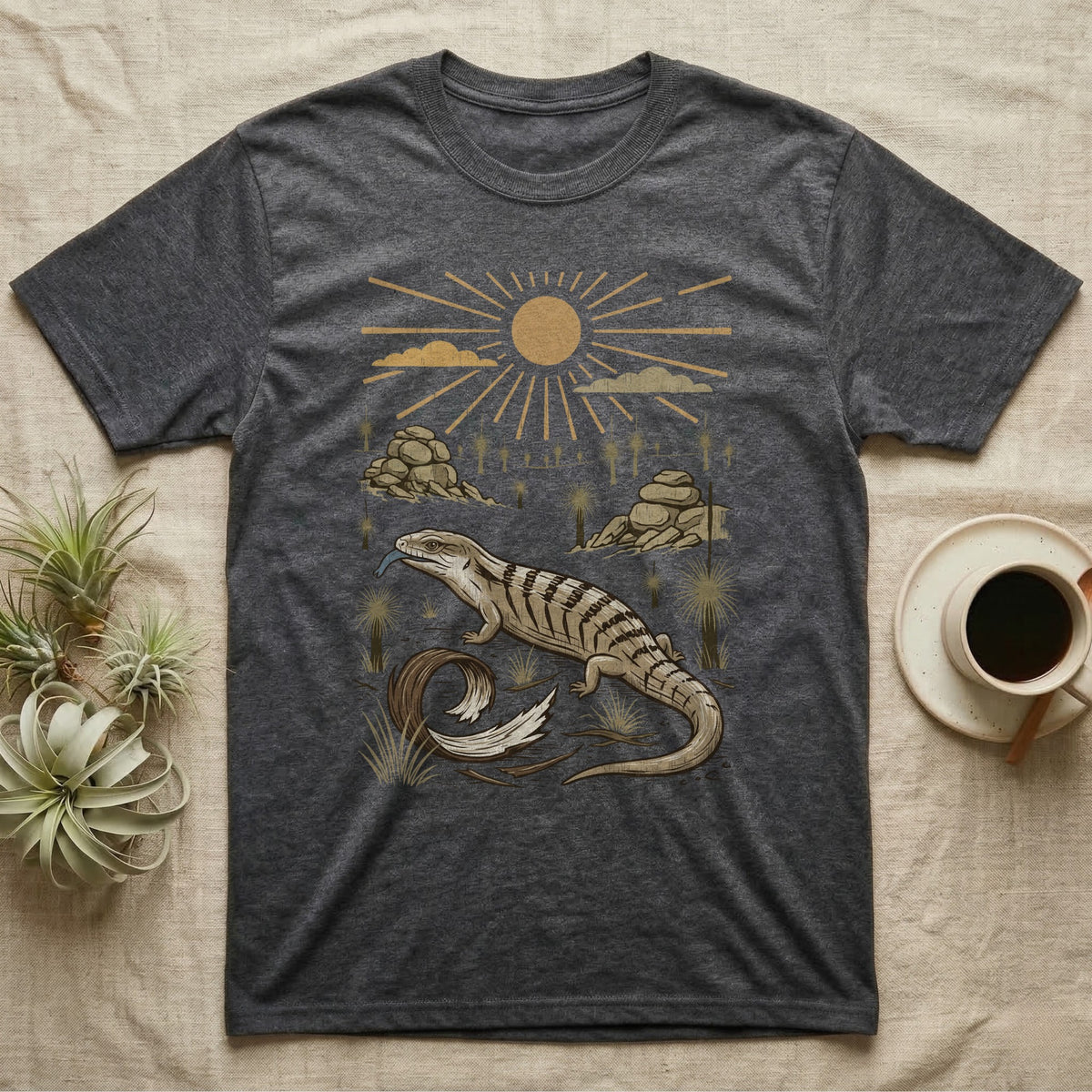 Blue-Tongued Skink Home Range T-Shirt in Dark Heather — Woodcut-style illustration of a blue-tongued skink walking across bare soil with its tongue out, shed skin and grass trees behind, no on-shirt text.
