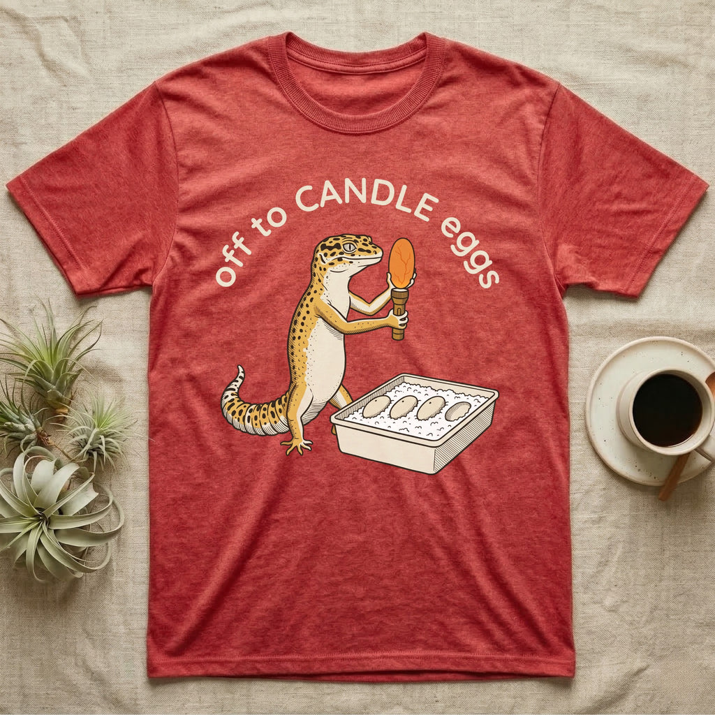 Leopard Gecko Candling T-Shirt in Heather Red — Leopard gecko holding a torch under a glowing orange egg beside a tub of eggs, under the words off to CANDLE eggs