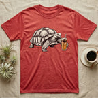 Slow Drip Tortoise T-Shirt in Heather Red — Flat meme-style illustration of a sulcata tortoise reaching slowly toward a tall iced slow-drip coffee.