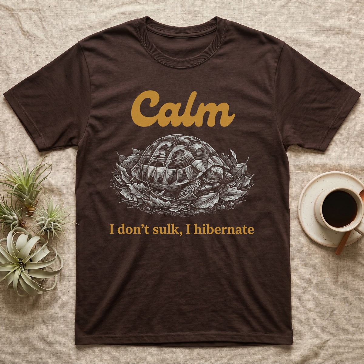 Hermann's Tortoise Calm T-Shirt in Dark Chocolate — White-line engraving of a Hermann's tortoise tucked into its shell in dry leaves under the word Calm