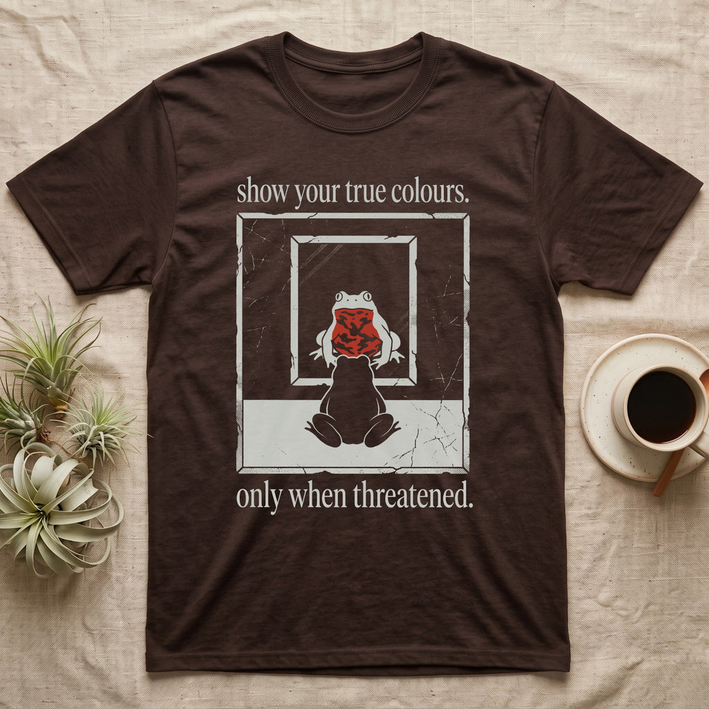 Fire-Bellied Toad Mirror T-Shirt in Dark Chocolate — Worn photocopy-style poster of a fire-bellied toad seen from behind looking into a mirror, its reflection showing a bright red marbled belly, with the words show your true colours, only when threatened.