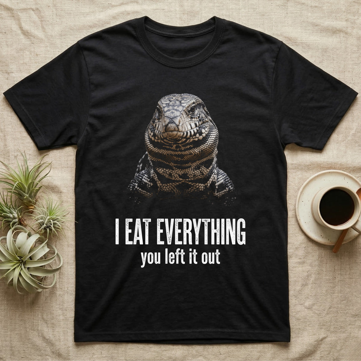 Deadpan photographic mugshot of an Argentine tegu facing the camera above the distressed text I Eat Everything, you left it out. — shown on a Black tee.