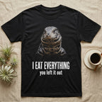 Deadpan photographic mugshot of an Argentine tegu facing the camera above the distressed text I Eat Everything, you left it out. — shown on a Black tee.
