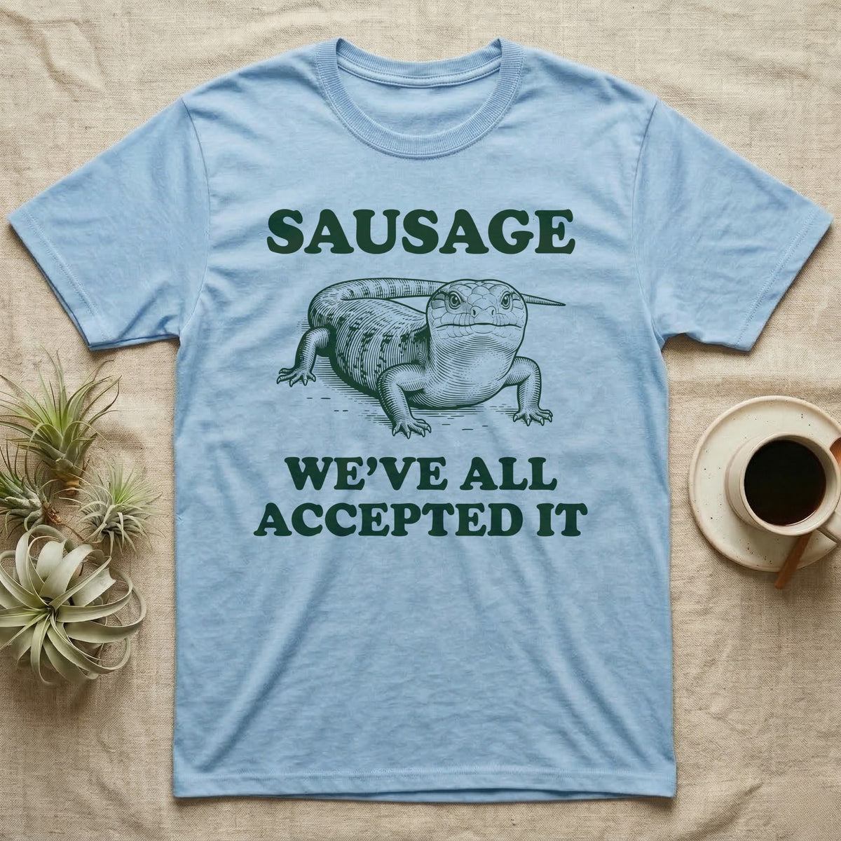 Blue Tongue Skink Sausage T-Shirt in Light Blue — Antique-engraved blue-tongued skink facing forward, with the word SAUSAGE above and a two-line caption below.