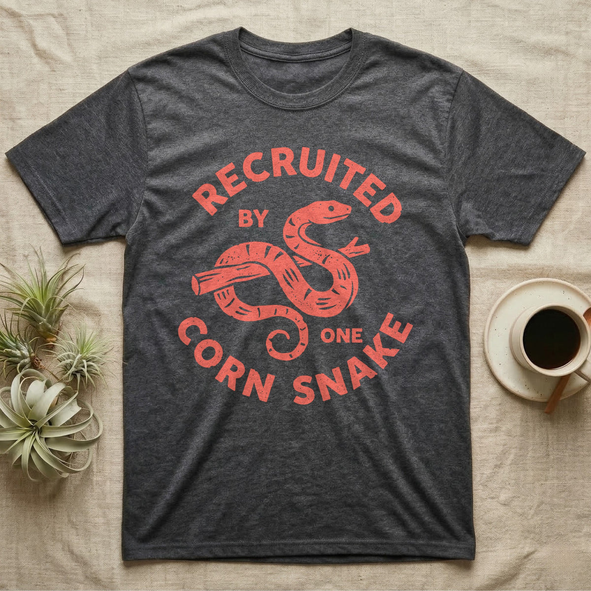 Corn Snake Recruit T-Shirt in Dark Heather — Hand-carved block-print badge of a corn snake on a branch inside ring lettering reading Recruited By One Corn Snake.