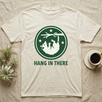 Cream t-shirt with raccoon hanging from branch and text "HANG IN THERE".