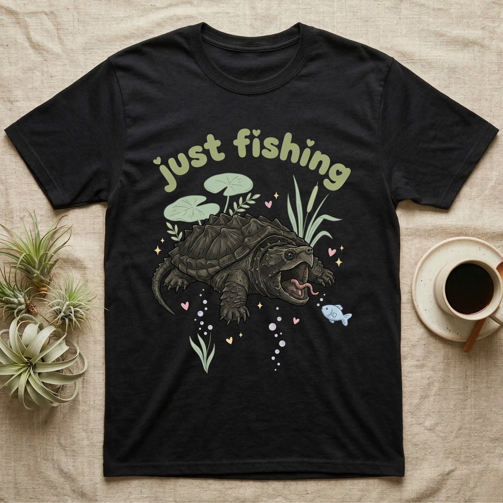 Alligator Snapping Turtle Softie T-Shirt in Black — Alligator snapping turtle with open mouth and tongue lure under a puffy pastel "just fishing" bubble wordmark.