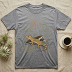 Leopard Gecko Home Range T-Shirt in Sport Grey — Woodcut-style illustration of a leopard gecko standing on cracked earth beside flat stones with thorn scrub behind, no on-shirt text.
