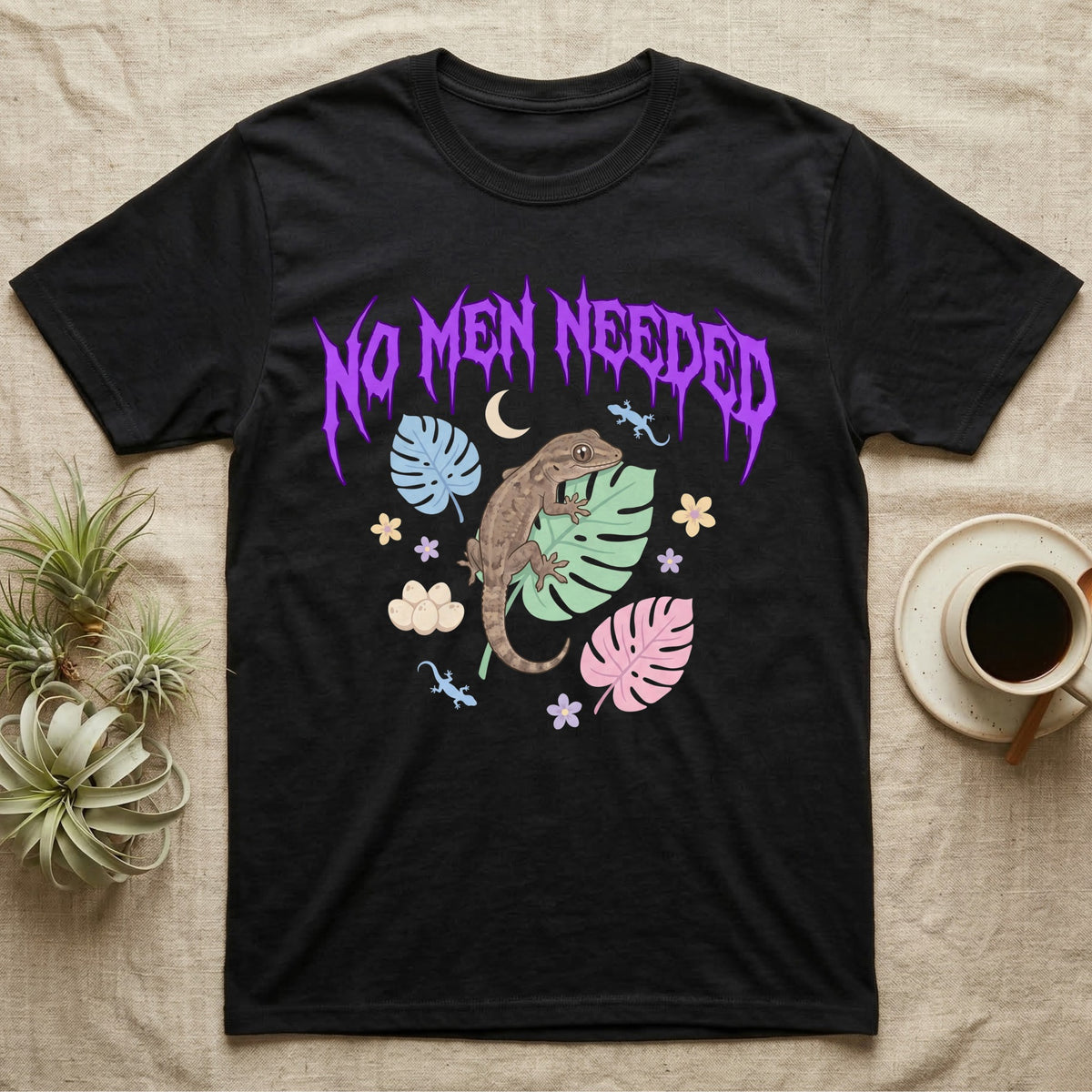 Mourning Gecko Feral T-Shirt in Black — Mourning gecko on a leaf flanked by clone silhouettes under a jagged violet metal "NO MEN NEEDED" wordmark.
