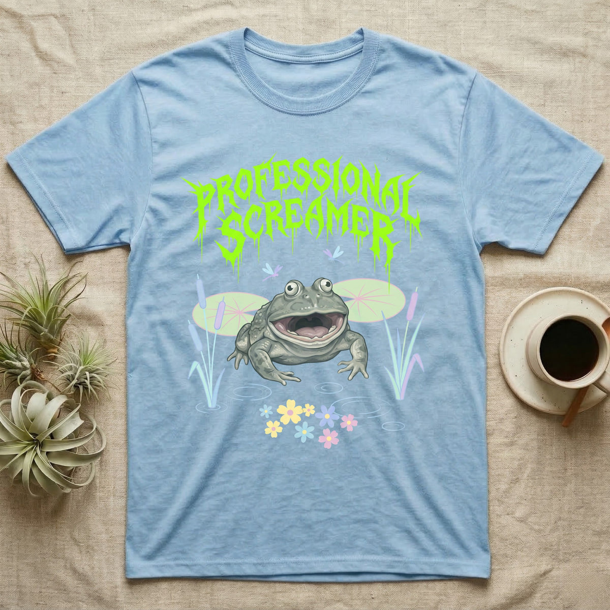 Budgett's Frog Feral T-Shirt in Light Blue — Budgett's frog with wide screaming mouth under jagged acid-green metal text PROFESSIONAL SCREAMER with lily pads