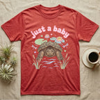 Common Snapping Turtle Baby T-Shirt in Heather Red — Snapping turtle with hooked beak and spiky shell among pastel lily pads under puffy pink bubble text "just a baby".