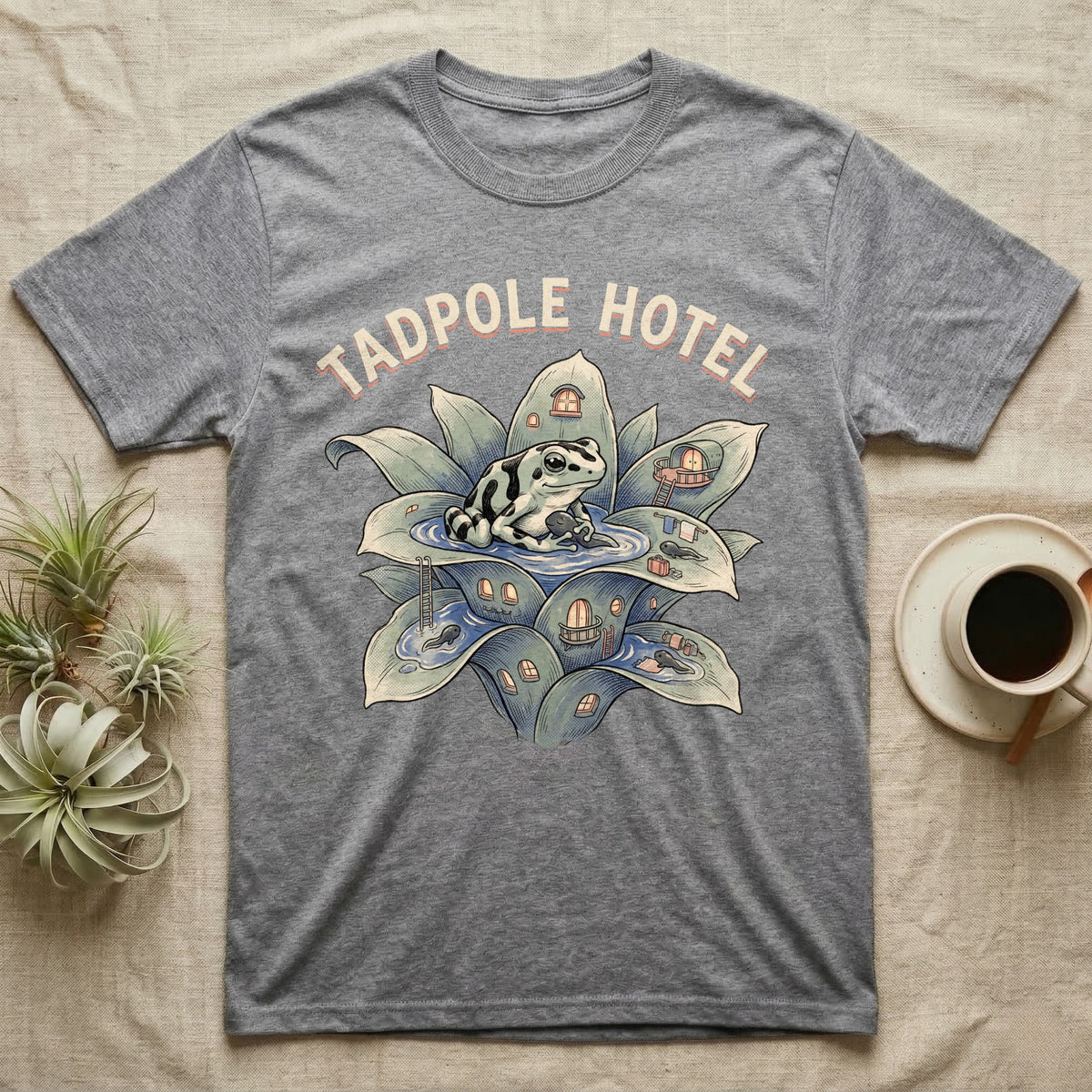 Tadpole Hotel Frog T-Shirt in Sport Grey — Whimsical naturalist illustration of a dart frog tucking tadpoles into a bromeliad Tadpole Hotel with hand-lettered marquee text.