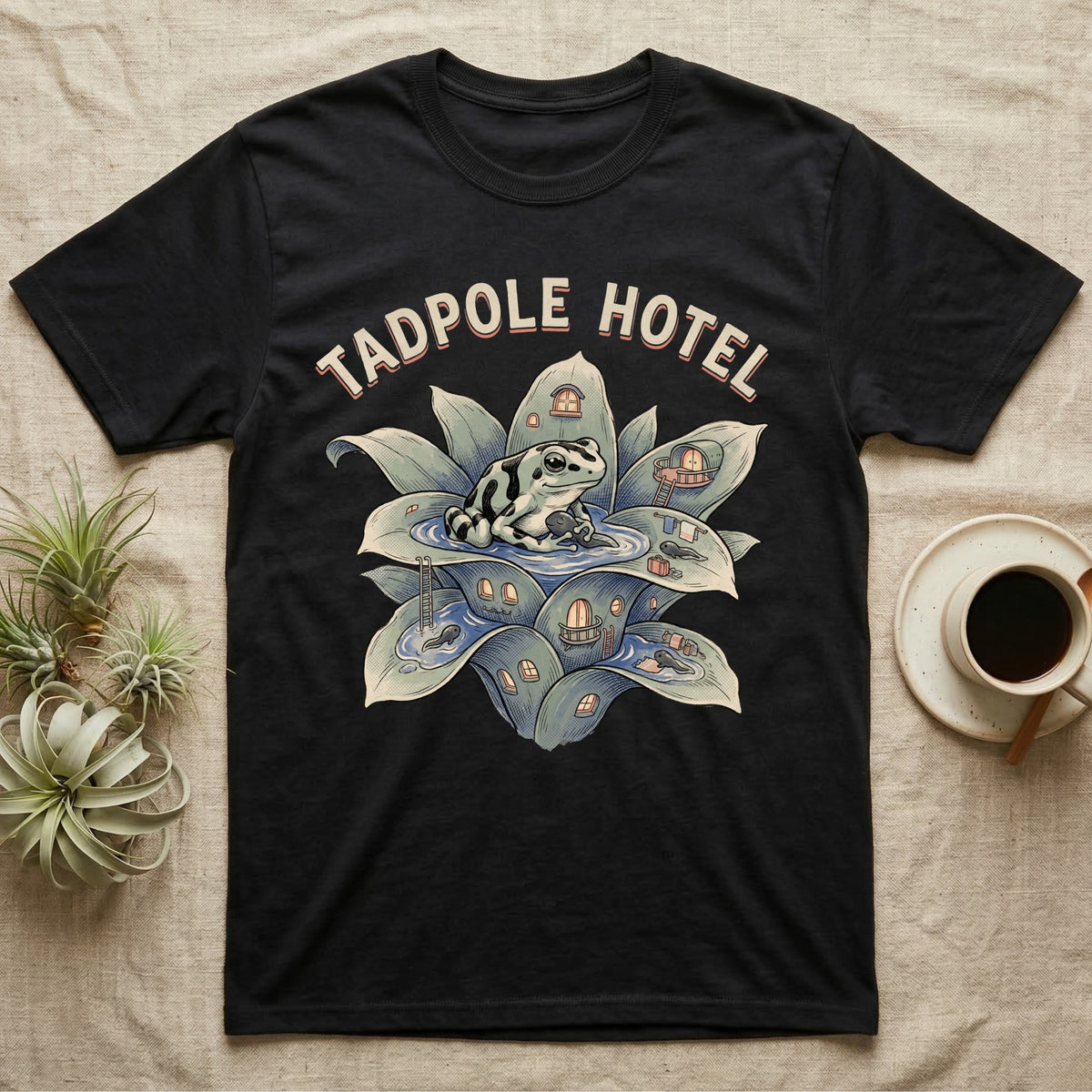 Tadpole Hotel Frog T-Shirt in Black — Whimsical naturalist illustration of a dart frog tucking tadpoles into a bromeliad Tadpole Hotel with hand-lettered marquee text.