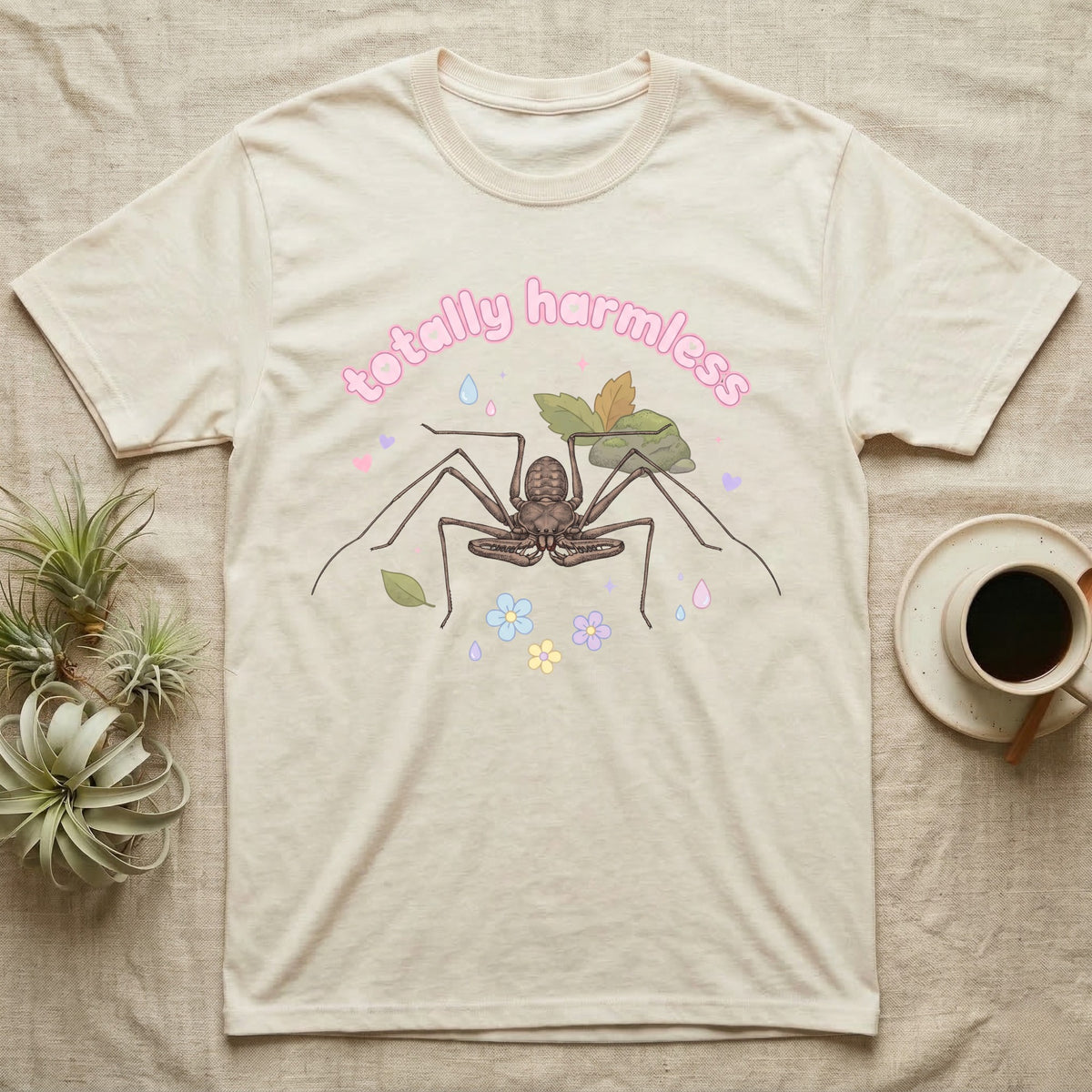 Tailless Whip Scorpion Baby T-Shirt in Natural — Pastel tailless whip scorpion with long whip legs among leaves and blossoms, puffy pink wordmark "totally harmless" above.