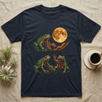 Fire-Bellied Toad Moon T-Shirt in Navy — Three fire-bellied toads under a glowing amber full moon, one on a mossy ledge, one reaching a front foot up at the moon