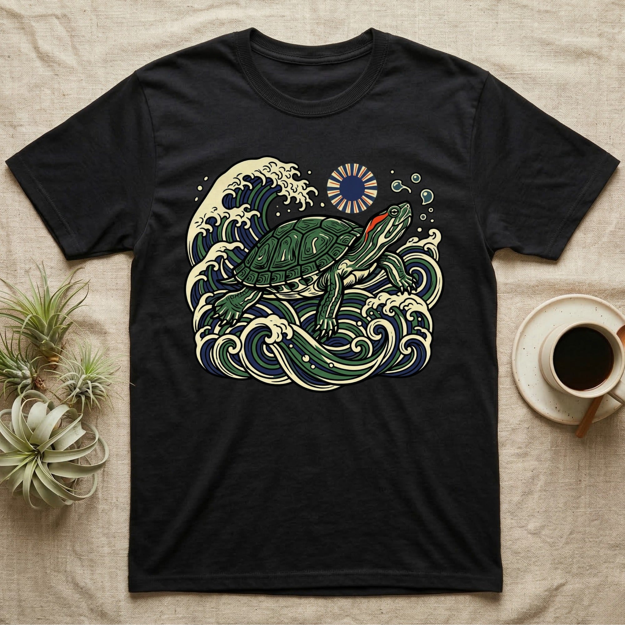Black t-shirt with a green sea turtle in stylized waves under a red sun.
