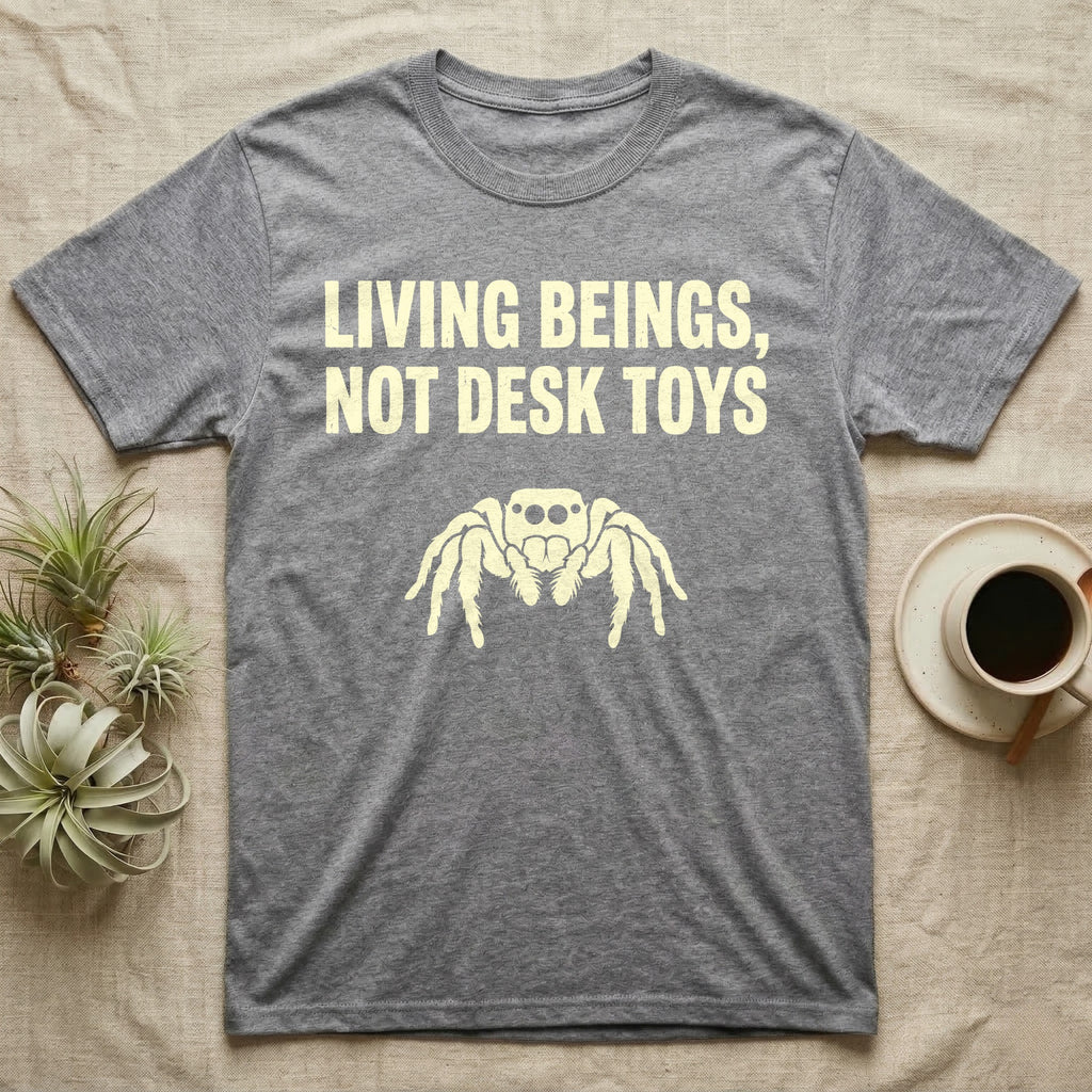 Living Beings Spider T-Shirt in Sport Grey — Bold typographic broadside reading Living Beings Not Desk Toys above a small front-facing jumping spider silhouette.