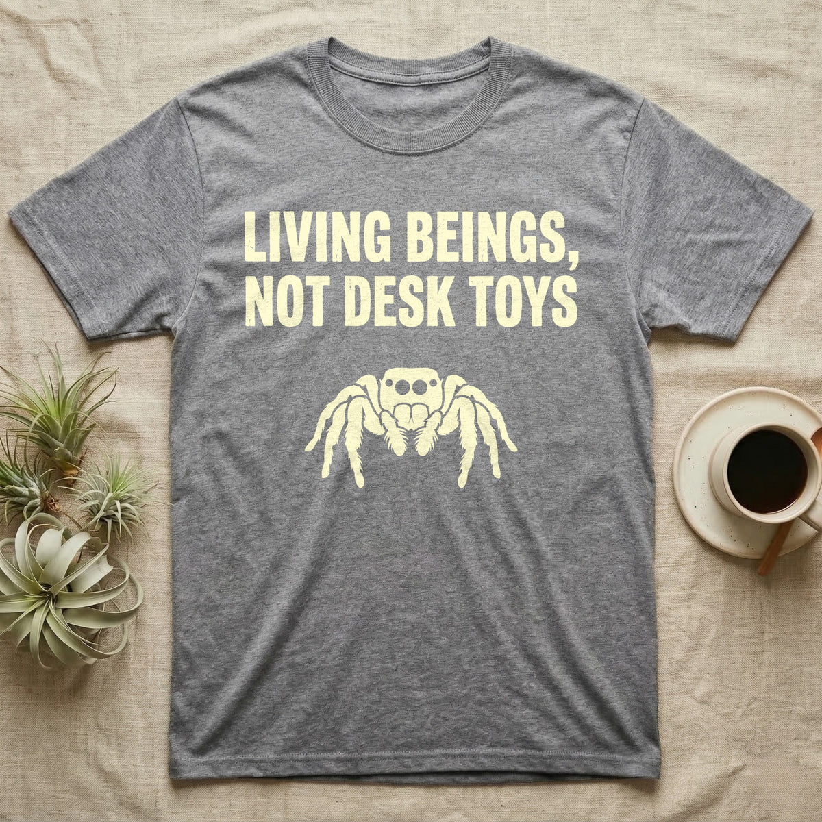 Living Beings Spider T-Shirt in Sport Grey — Bold typographic broadside reading Living Beings Not Desk Toys above a small front-facing jumping spider silhouette.
