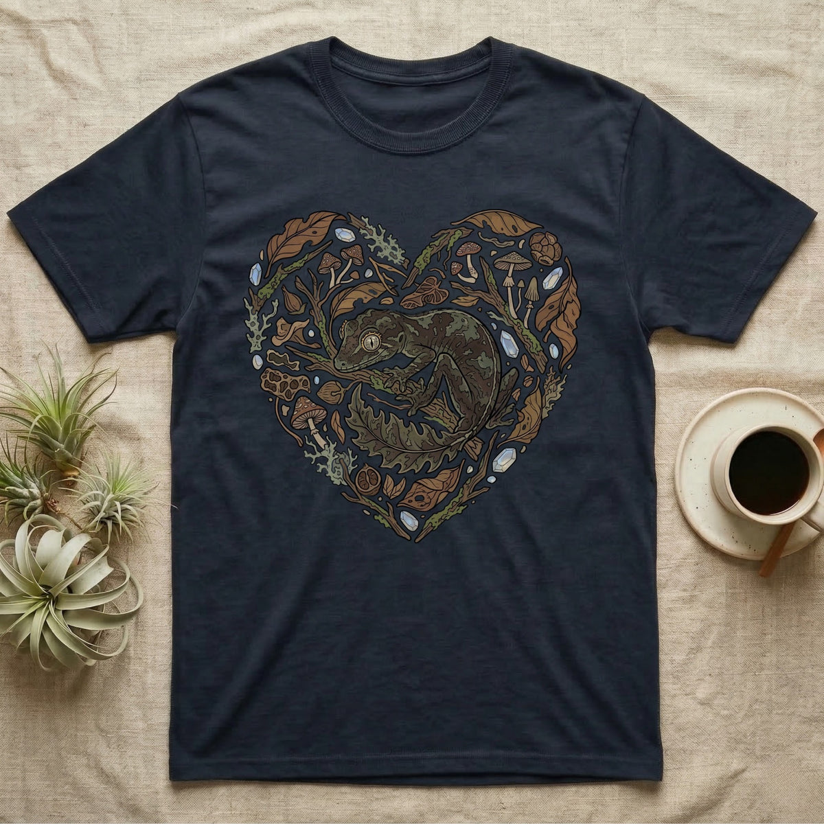 Dark t-shirt with a heart-shaped graphic of a gecko surrounded by leaves and mushrooms.