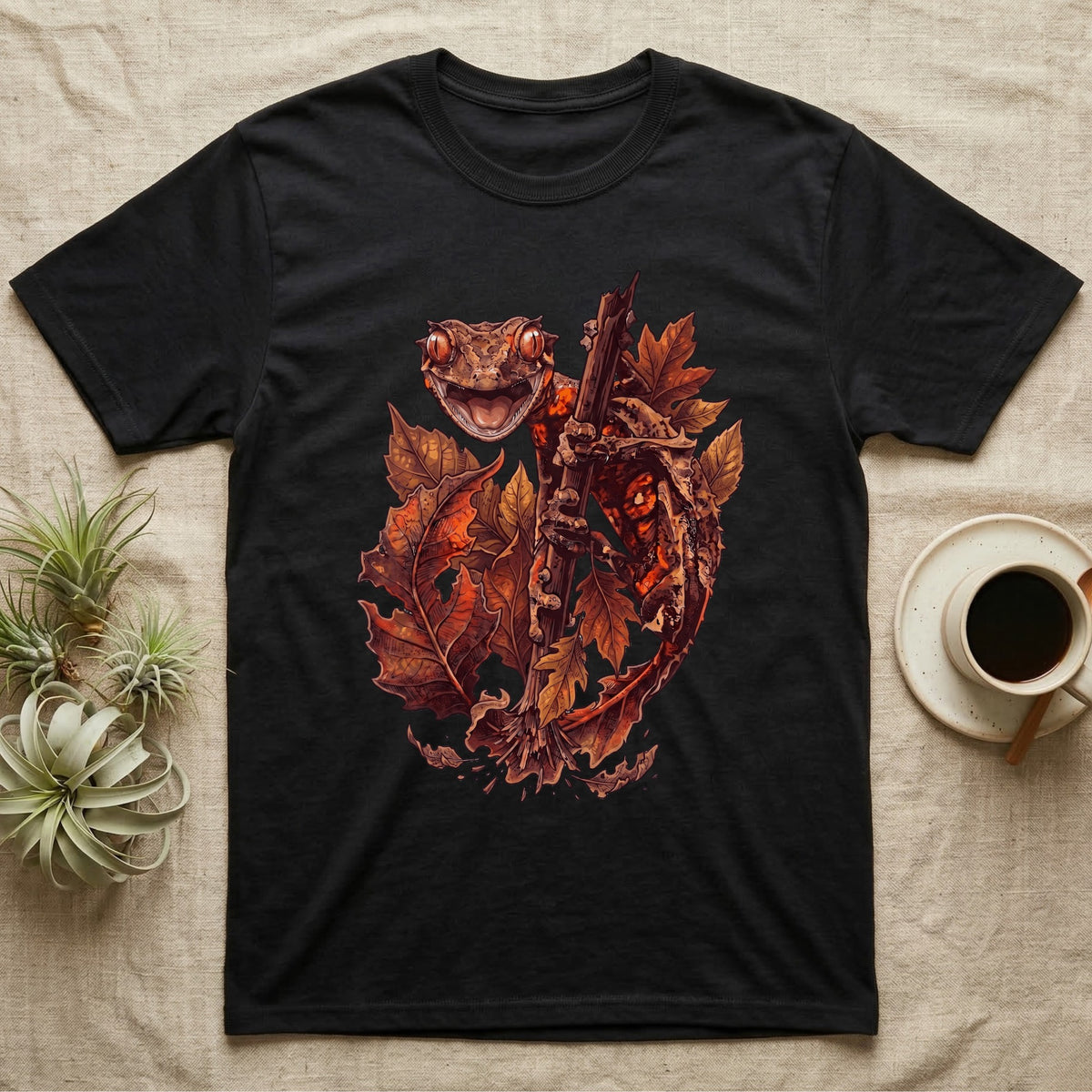 Satanic Leaf-Tailed Gecko Autumn T-Shirt in Black — Painted illustration of a satanic leaf-tailed gecko gripping a bare stem among dried autumn leaves in rust and amber, no on-shirt text.