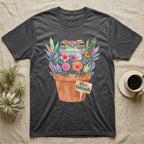 Tree Frog Thriving T-Shirt in Dark Heather — A White's tree frog made of watercolour flowers, sitting in a terracotta pot with a plant label reading STILL THRIVING.